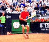 a man in a red shirt is holding a tennis racquet on a court with a bnp logo in the background