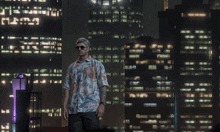 a man in a hawaiian shirt is standing in front of a city at night