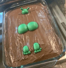 a chocolate cake decorated to look like shrek is in a glass pan on a counter .