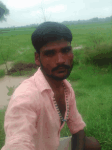 a man in a pink shirt is sitting in a grassy field