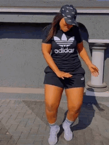 a woman wearing a black adidas t-shirt and black shorts is standing on a sidewalk .