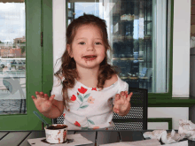 a little girl sitting at a table with a cup of chocolate ice cream in front of her