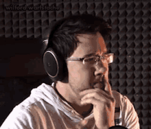 a man wearing headphones and glasses is sitting in front of a microphone and thinking .