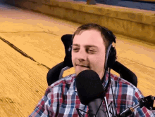 a man wearing headphones and a plaid shirt talks into a microphone