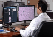 a man in a lab coat is sitting in front of two computer monitors .