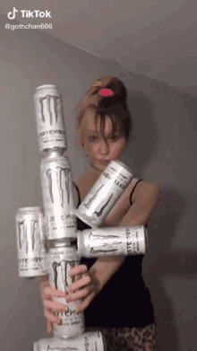 a girl is holding a stack of monster cans