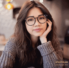 a woman wearing glasses and a sweater has her hand resting on her face