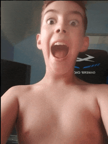 a shirtless boy is taking a selfie in front of a gaming chair that says x