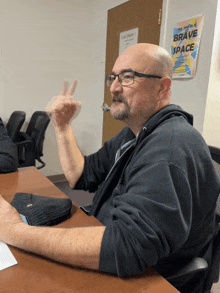 a bald man sits at a table with a sign that says brave space