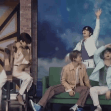 a group of young men are sitting on a green couch and dancing .