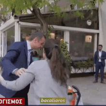 a man in a suit and tie is talking to a woman in a wheelchair in front of a building that says bacaliaro