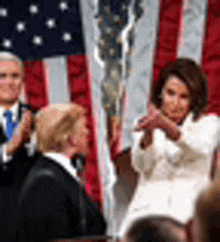 a woman is giving a speech in front of an american flag while two men are applauding .