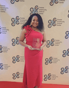 a woman in a red dress is holding an award in front of a backdrop that says cazale community cultural center