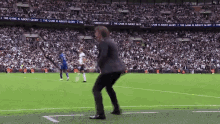 a man in a suit is dancing on a soccer field in front of a banner that says the game is about glory