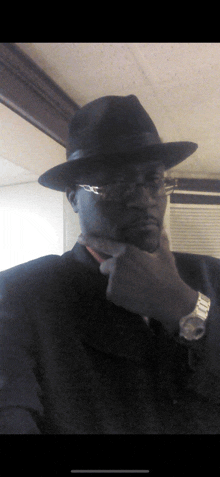 a man wearing a hat and glasses is holding his hand to his chin