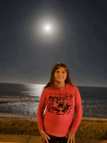 a woman in a red sweater with a tiger on it stands in front of the ocean