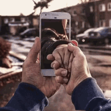 a person is holding a cell phone in their hands and taking a picture of a couple 's hands .