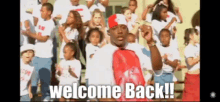 a man in a red hat stands in front of a crowd with the words welcome back written on the bottom