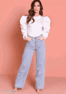 a woman is wearing a white sweater and wide leg jeans .