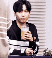 a young man is sitting at a table holding a cup of coffee with a straw in his mouth .