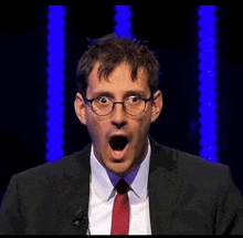 a man wearing glasses and a suit is making a surprised face on a stage .