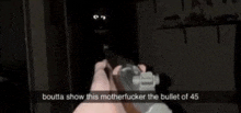 a person is holding a gun in their hand in a dark room with a bullet of 45 in the background .