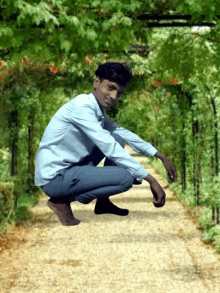 a young man in a blue shirt is squatting on a path