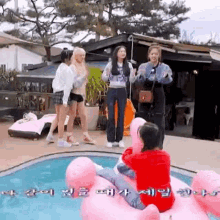 a group of girls are standing around a swimming pool . one of the girls is sitting on a pink float .