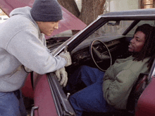 a man talking to another man in a car with the hood up