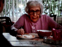 an elderly woman sits at a table with a plate of food and a caption that says cream cheese on toast