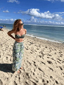 a woman in a bikini stands on a sandy beach near the ocean