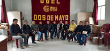 a group of men are sitting in front of a sign that says dos de mayo