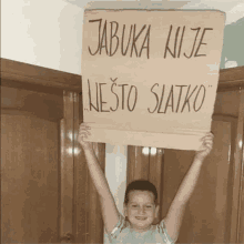 a young boy is holding up a cardboard sign that says jabuka nije