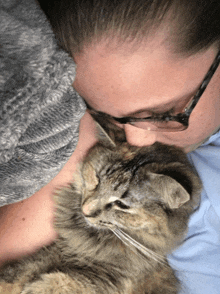 a woman wearing glasses is hugging a cat