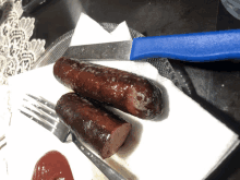 two sausages on a napkin next to a knife and ketchup