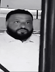 a black and white photo of a man with a beard wearing a white shirt standing in a room .