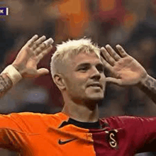 a soccer player is raising his hands in the air while wearing an orange and maroon jersey .