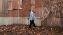 a man wearing a red hat walks in front of a wall with a painting of an angel on it