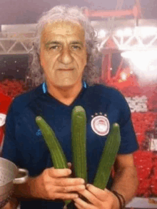 a man wearing a blue shirt is holding three cucumbers .