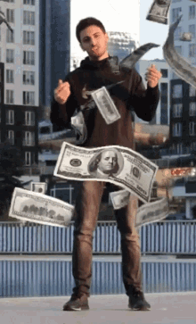 a man in a black hoodie is surrounded by hundred dollar bills flying in the air