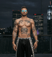 a shirtless man with a tattoo on his chest is wearing sunglasses and shorts that say kappa