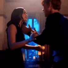 a man and a woman are dancing in a dark room . the woman is wearing a black dress .