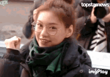 a girl wearing glasses and a green scarf is making a heart with her hands .