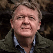 a close up of an older man wearing a green jacket and a blue shirt .