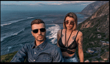 a man and a woman wearing sunglasses are standing on top of a mountain overlooking the ocean