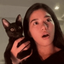 a woman is holding a black cat in her hands