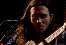 a man with long hair is singing into a microphone while holding a guitar .