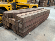 a stack of wooden blocks sits in front of a yellow forklift in a warehouse