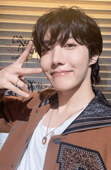 a young man wearing a brown jacket and a white shirt giving the peace sign