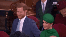 a man in a suit and tie is sitting next to a woman in a green hat with the words bbc studios on the bottom right